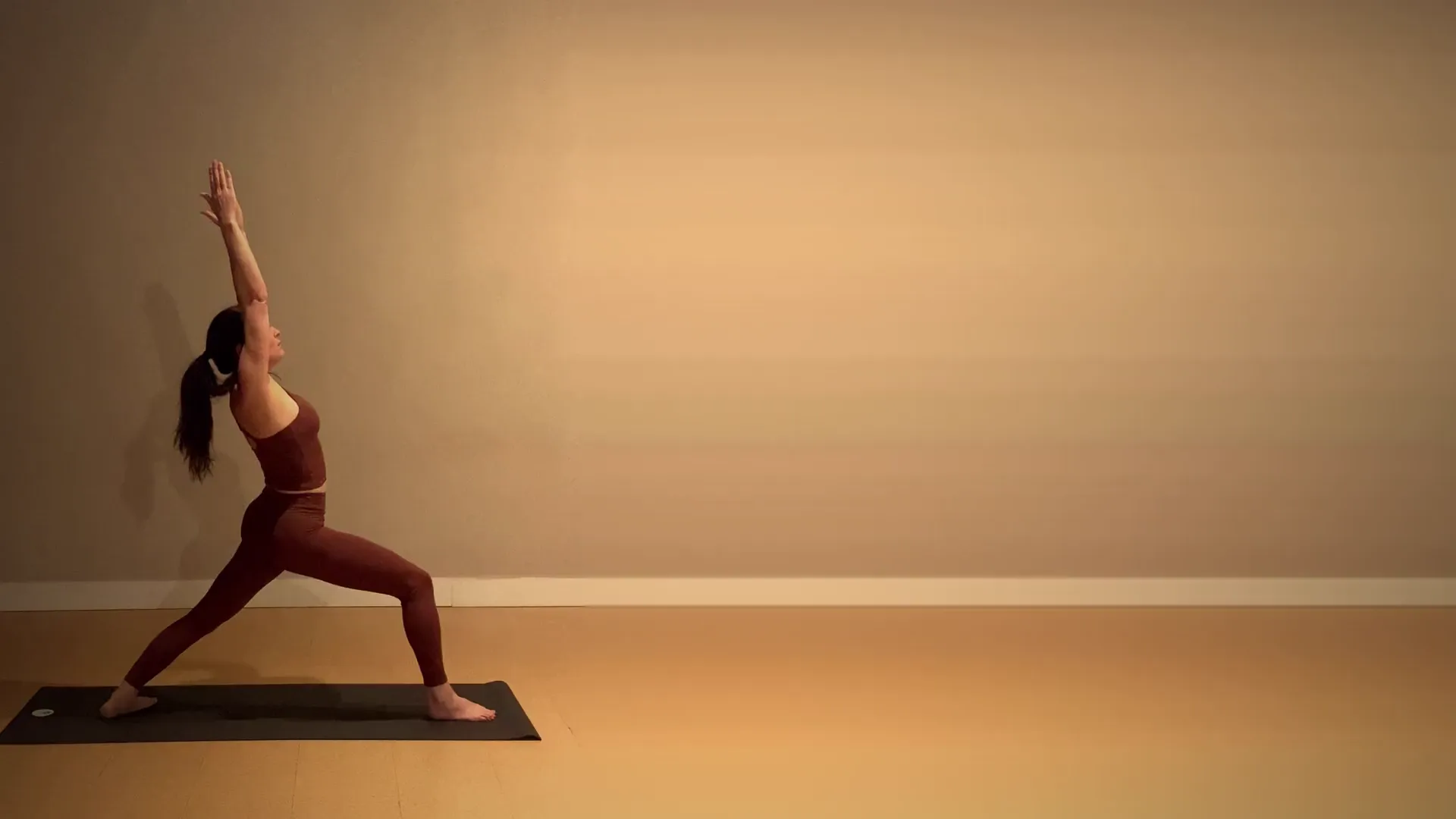 A student in Warrior I, arms overhead, on her mat at 3B Movement